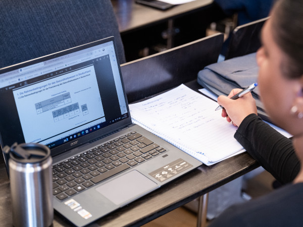 Studentin hält Notizen und schaut die Folien.